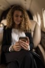 Beautiful businesswoman using mobile phone in private jet — Stock Photo