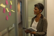 Reife Geschäftsfrau blickt im Büro mit einem klebrigen Zettel an die Wand — Stockfoto