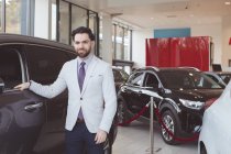 Portrait of confident salesman standing next to car — Stock Photo