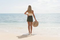 Вид ззаду жінка тримає капелюх на пляжі — стокове фото