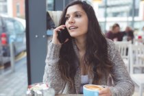 Жінка розмовляє по мобільному телефону, маючи каву в кав'ярні — стокове фото