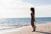 Жінка стоїть з дошкою для серфінгу на пляжі в сонячний день — стокове фото