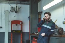 Механик разговаривает по мобильному телефону в ремонтном гараже — стоковое фото
