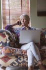 Зрелая женщина разговаривает по мобильному телефону, используя ноутбук дома — стоковое фото