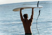 Vista posteriore del surfista maschio che cammina con la tavola da surf in spiaggia — Foto stock