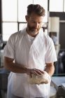 Mature male baker holding a dough in bakery shop — Stock Photo