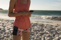 Jogadora de voleibol feminina usando telefone celular na praia — Fotografia de Stock