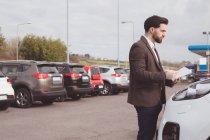 Verkäufer steht neben Auto und liest Broschüre vor dem Verkaufsraum — Stockfoto
