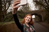 Beautiful woman taking selfie with mobile phone in countryside road — Stock Photo