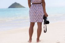 Вид сзади женщины, стоящей с цифровой камерой на пляже — стоковое фото