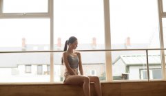 Задумчивая танцовщица отдыхает у окна в танцевальной студии — стоковое фото