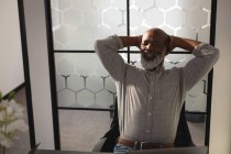 Старший графический дизайнер расслабляется с руками за головой в офисе — стоковое фото