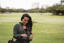 Улыбающаяся женщина использует стеклянный цифровой планшет в парке — стоковое фото