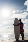 Rear view of male surfer standing with surfboard in the beach — Stock Photo