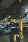 Mecánico masculino examinando un coche con antorcha en garaje de reparación - foto de stock