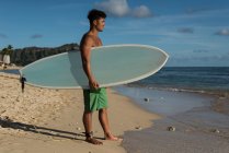 Молодий чоловік-серфер стоїть з дошкою для серфінгу на пляжі — стокове фото