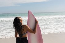 Vista posteriore di surfista donna in piedi con tavola da surf in spiaggia — Foto stock