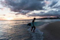 Surfeur masculin debout avec planche de surf à la plage au crépuscule — Photo de stock