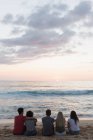 Grupo de amigos sentados juntos na praia ao entardecer — Fotografia de Stock