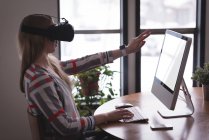 Female executive using virtual reality headset with computer at desk in office — Stock Photo