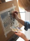 Artista feminina pintando em uma tela com um pincel e segurando uma paleta de cores em casa — Fotografia de Stock