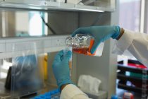 Scientifique versant la solution chimique sur le tube à essai de la bouteille dans le laboratoire — Photo de stock