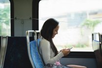 Усміхнена жінка використовує мобільний телефон під час подорожі в автобусі — стокове фото