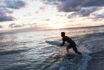Surfeur masculin surfant avec planche de surf dans la mer au crépuscule — Photo de stock