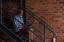 Старший использует ноутбук на лестнице дома — стоковое фото