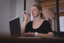 Женщина-руководитель разговаривает по мобильному телефону во время работы на ноутбуке в офисе — стоковое фото