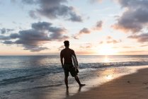Мужчина-серфер стоит с доской для серфинга на пляже в сумерках — стоковое фото