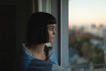 Nachdenkliche Frau schaut zu Hause durch Fenster — Stockfoto