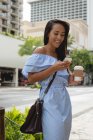 Усміхнена красива жінка використовує мобільний телефон, маючи каву на вулиці — стокове фото