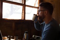 Hombre en cabaña de madera con taza de café mirando a través de la ventana - foto de stock
