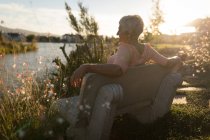 Seniorin entspannt sich an sonnigem Tag auf Bank am Flussufer — Stockfoto