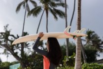 Mujer caminando con tabla de surf en la playa en un día soleado - foto de stock
