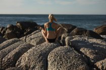 Rückansicht einer Volleyballerin, die am Strand Yoga auf dem Felsen macht — Stockfoto