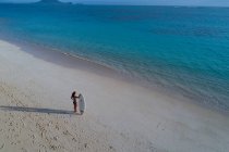 Donna con tavola da surf in piedi sulla spiaggia e guardando il mare — Foto stock