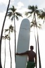 Vue arrière de l'homme debout avec planche de surf sur la plage — Photo de stock