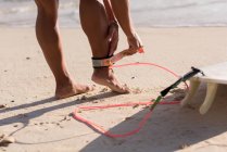 Donna che indossa guinzaglio tavola da surf sulla gamba in spiaggia — Foto stock