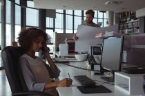 Жінка-архітектор розмовляє по телефону, коли колега перевіряє план в офісі — стокове фото