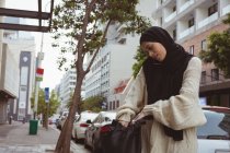 Beautiful hijab woman talking on mobile phone while checking her purse — Stock Photo