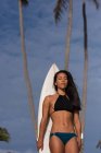 Mulher de pé com prancha de surf na praia em um dia ensolarado — Fotografia de Stock