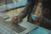 Seção média de mulher usando laptop enquanto toma café no café — Fotografia de Stock