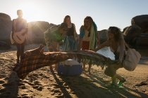 Group of friends laying down picnic blanket in the beach — Stock Photo