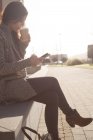 Жінка використовує мобільний телефон, маючи каву в сонячний день — стокове фото