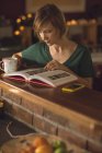 Красива жінка читає книгу, маючи каву вдома — стокове фото