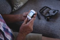 Старший чоловік перевіряє цукор в крові з глюкометром вдома — стокове фото