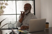 Senior graphic designer talking on mobile phone at desk in office — Stock Photo