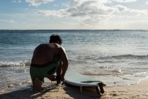 Surfista masculino amarrando coleira de prancha em sua perna na praia — Fotografia de Stock